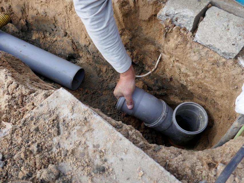person installing sewer pipe underground