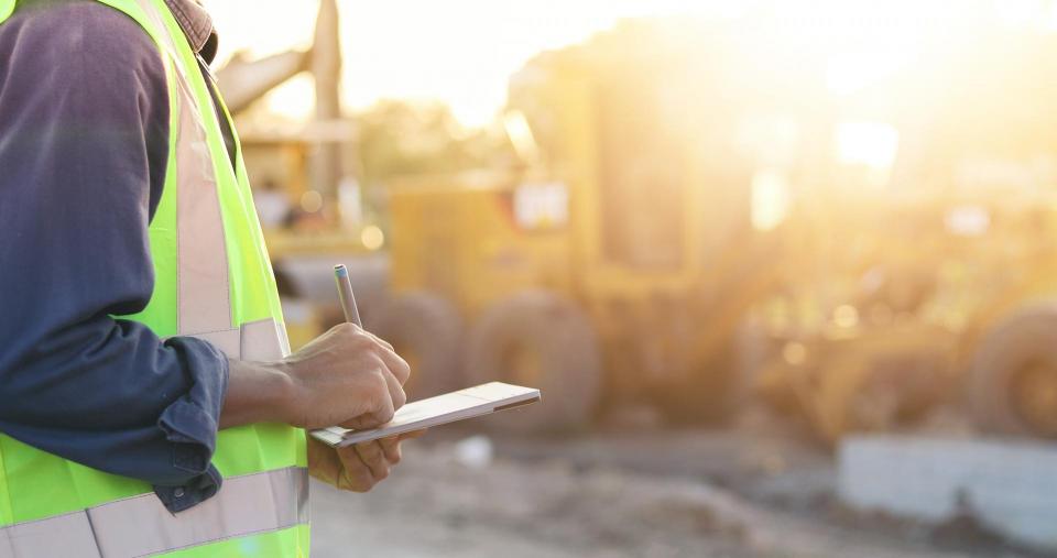 person in yellow vest looking at clipboard at construction site