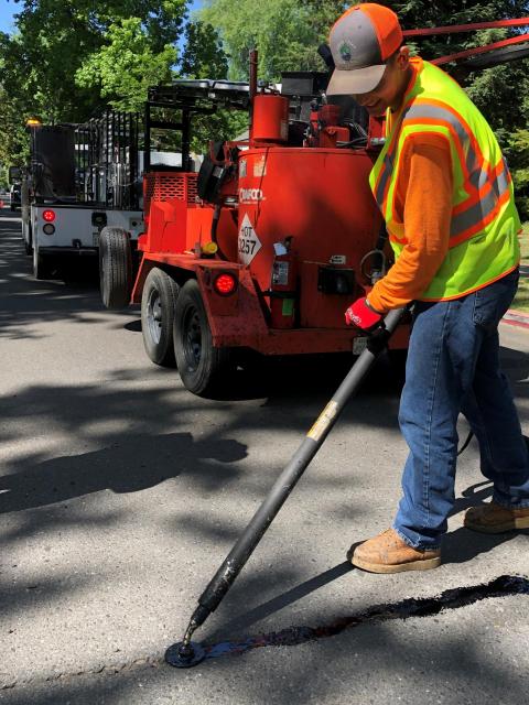 public works worker filling roadway with crackseal with red truck in background